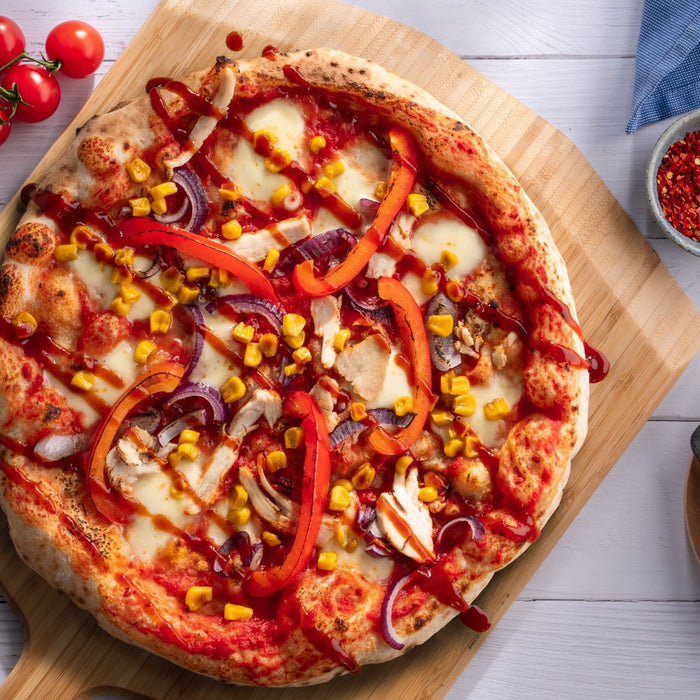 A pizza topped with peppers, chicken, sweetcorn and BBQ sauce on a wooden pizza peel. Baked using a BBQ chicken recipe. 