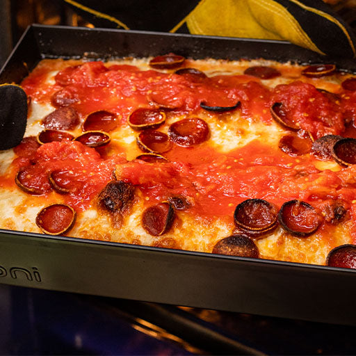 Detroit style pizza topped with tomatoes, cheese and pepperoni in a metal tray on a wooden chopping board. Baked using a Detroit Style Pizza recipe