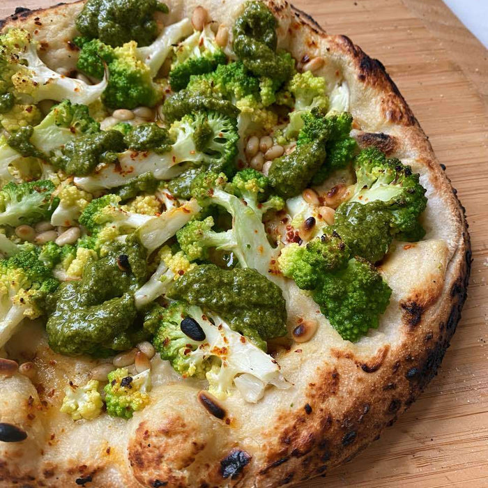 Romanesco Pizza with Cashew Cream, Salsa Verde and Pine Nuts on a wooden pizza peel