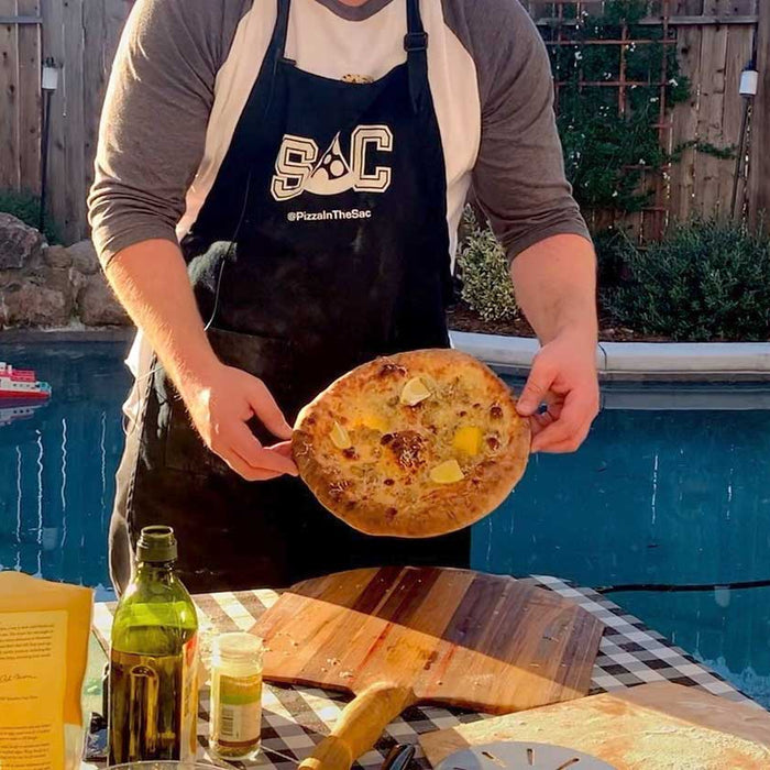 Chef holding a baked white clam pizza, made using a white clam pizza recipe.