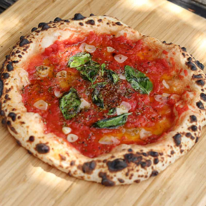 A pizza topped with tomatoes, basil and garlic on a wooden pizza peel. Baked using a marinara pizza recipe.