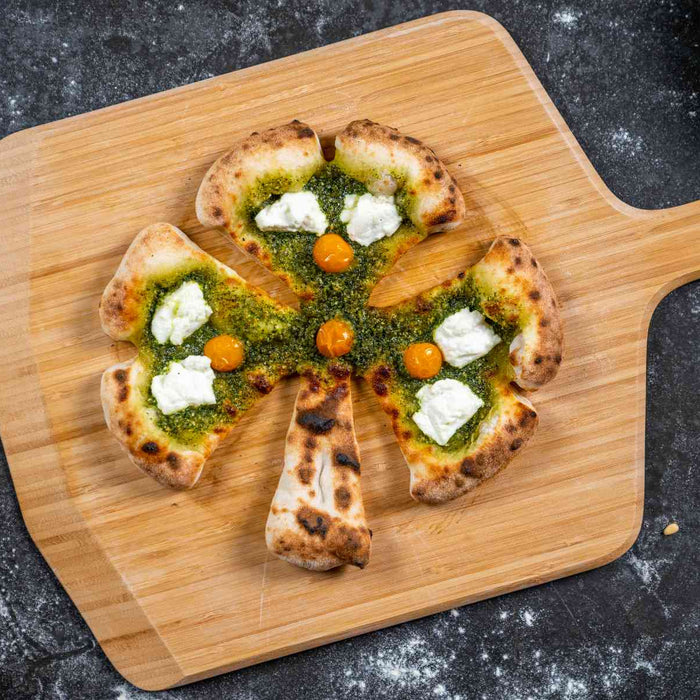 A pizza cut into a shape of a clover topped with pesto and ricotta on a wooden pizza peel