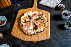 Finnish pizza with salmon, capers, pickeld onions, basil and crème fraîche on an Ooni Bamboo Pizza Peel.