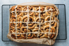 Hot cross Chelsea buns with an iced topping on a piece of parchment paper on a wire rack