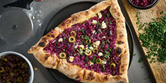 Hamantaschen Pizza with Caramelized Onions, Olives, Feta and Pomegranate Seeds