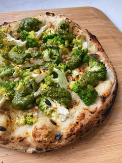 Romanesco Pizza with Cashew Cream, Salsa Verde and Pine Nuts on a wooden pizza peel