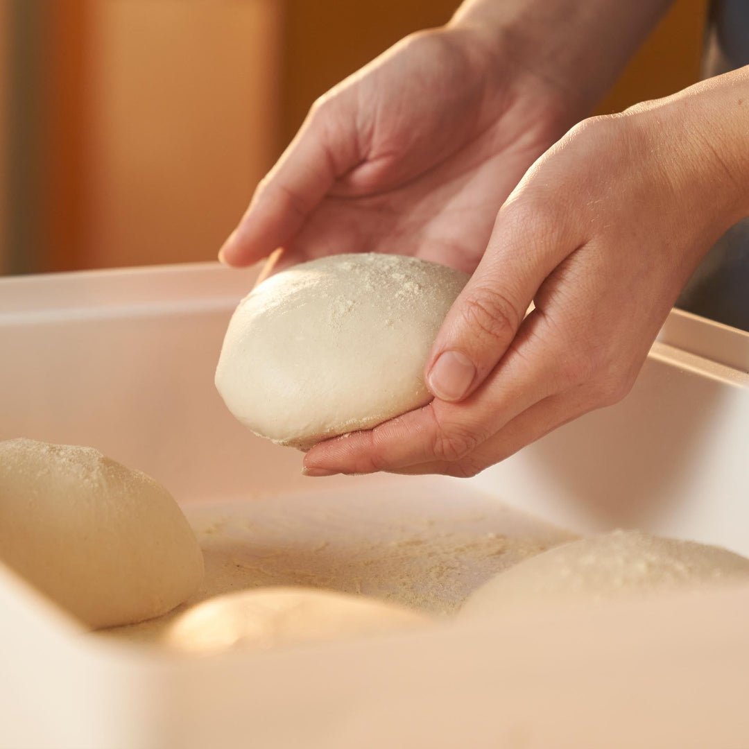 hands lowering pizza dough ball into ooni dough proofing boxes