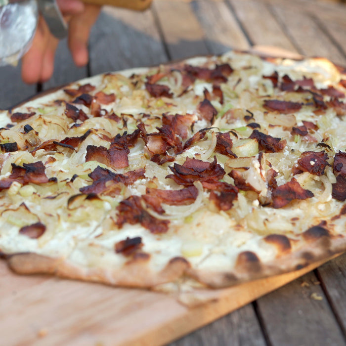 Traditional Flammkuchen on a wooden chopping board cooked using a Flammkuchen recipe