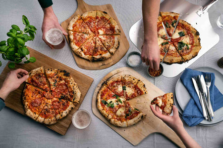 Several pizzas on wooden chopping boards on a table being shared