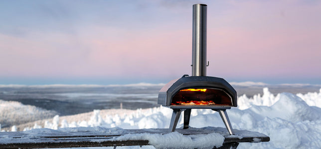 An Ooni Pizza Oven on a snow covered table on a backdrop of ice and snow in Lapland