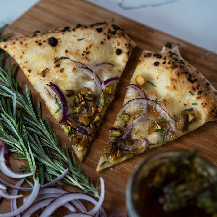 Two slices of pizza topped with pistachios and red onion on a wooden pizza peel with fresh rosemary