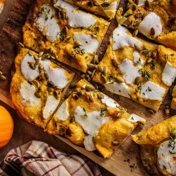 Protein-crust Pizza covered with Pumpkin, Thyme, and Ricotta on a wooden chopping board