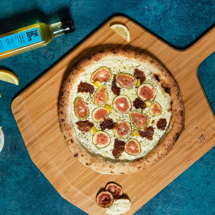 Pizza covered in feta, lemons and figs on a wooden pizza peel