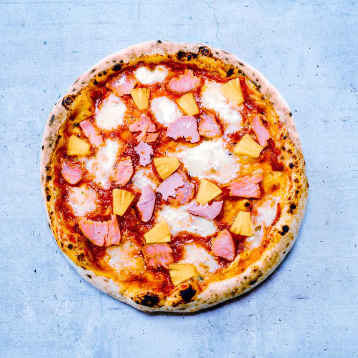 Hawaiian pizza topped with ham and pineapple on a blue table top