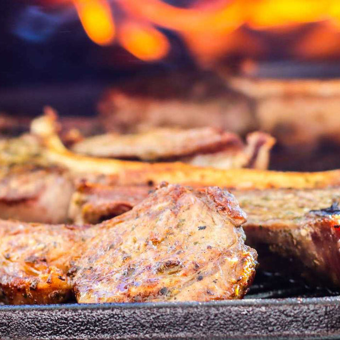 Lamb chops on a cast iron pan being grilled in an Ooni Karu 16 pizza oven
