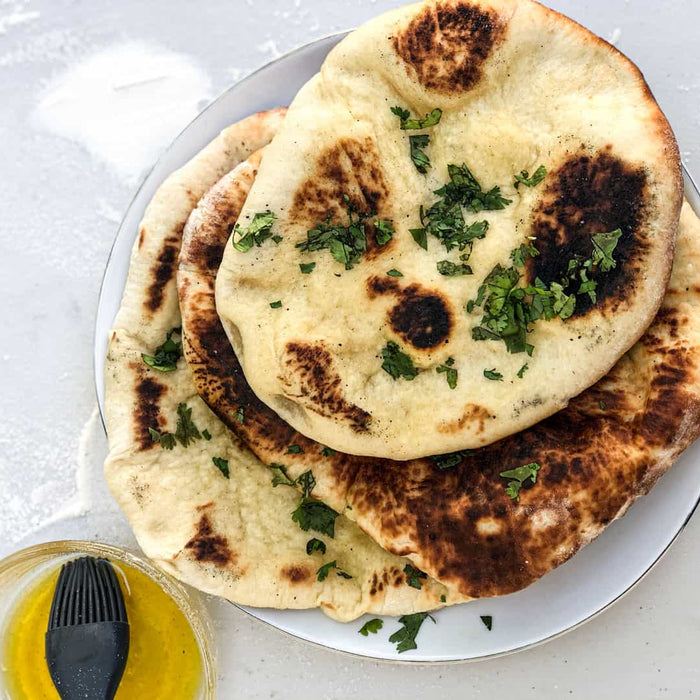 Sourdough naan breads on stacked on a white plate using a sourdough naan recipe