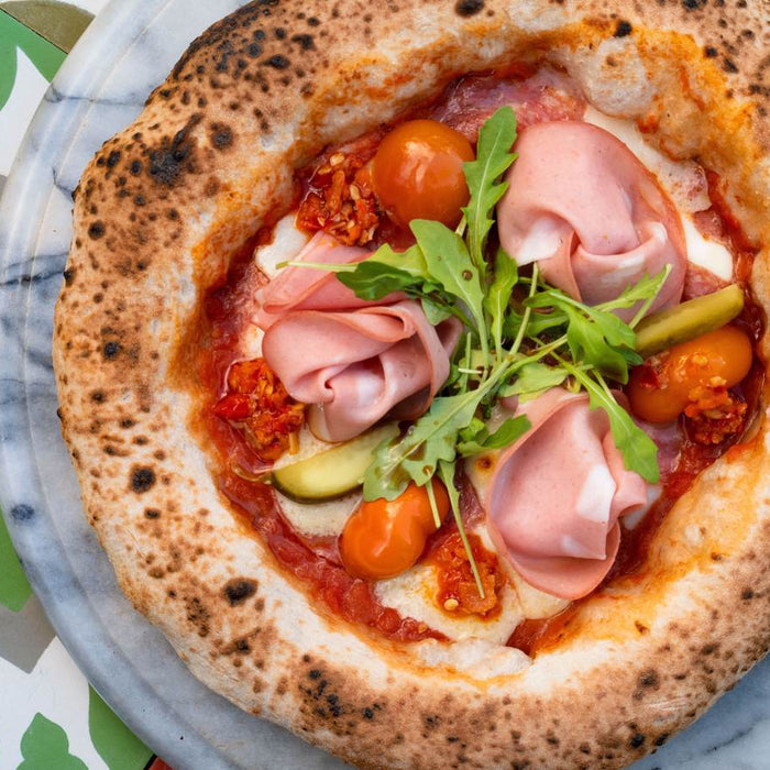 Pizza topped with spicy salami, ham and rocket on a plate