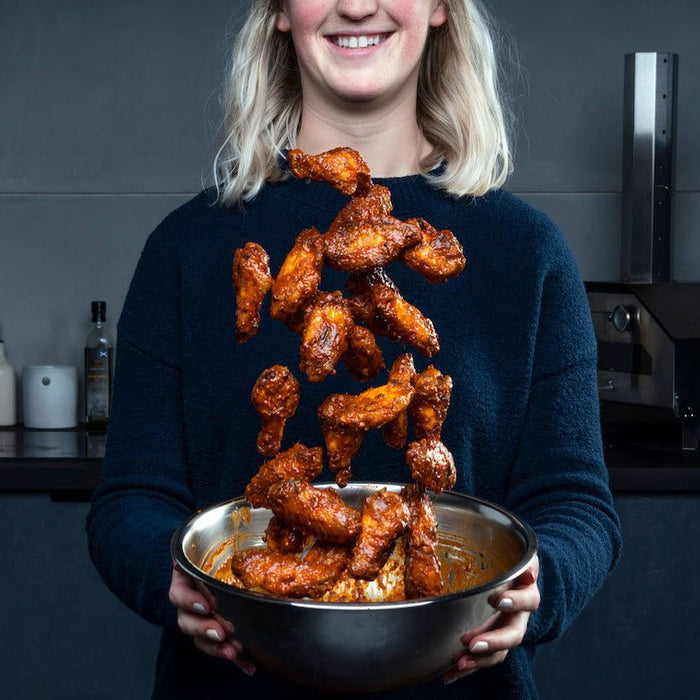 Female chef tossing wood-fired buffalo chicken wings in buffalo sauce in a metal bowl