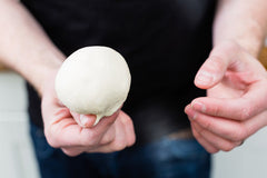 A pair of hands holding a pizza dough ball