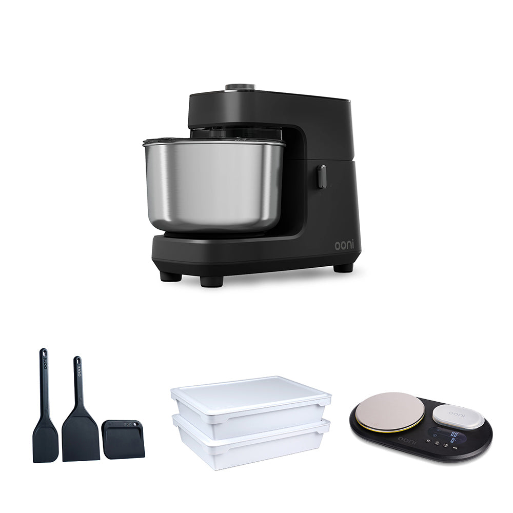 A black stand mixer with a stainless steel bowl is shown above three accessory items on a white background: two black spatulas, two white rectangular containers, and a black digital scale. #variant-1