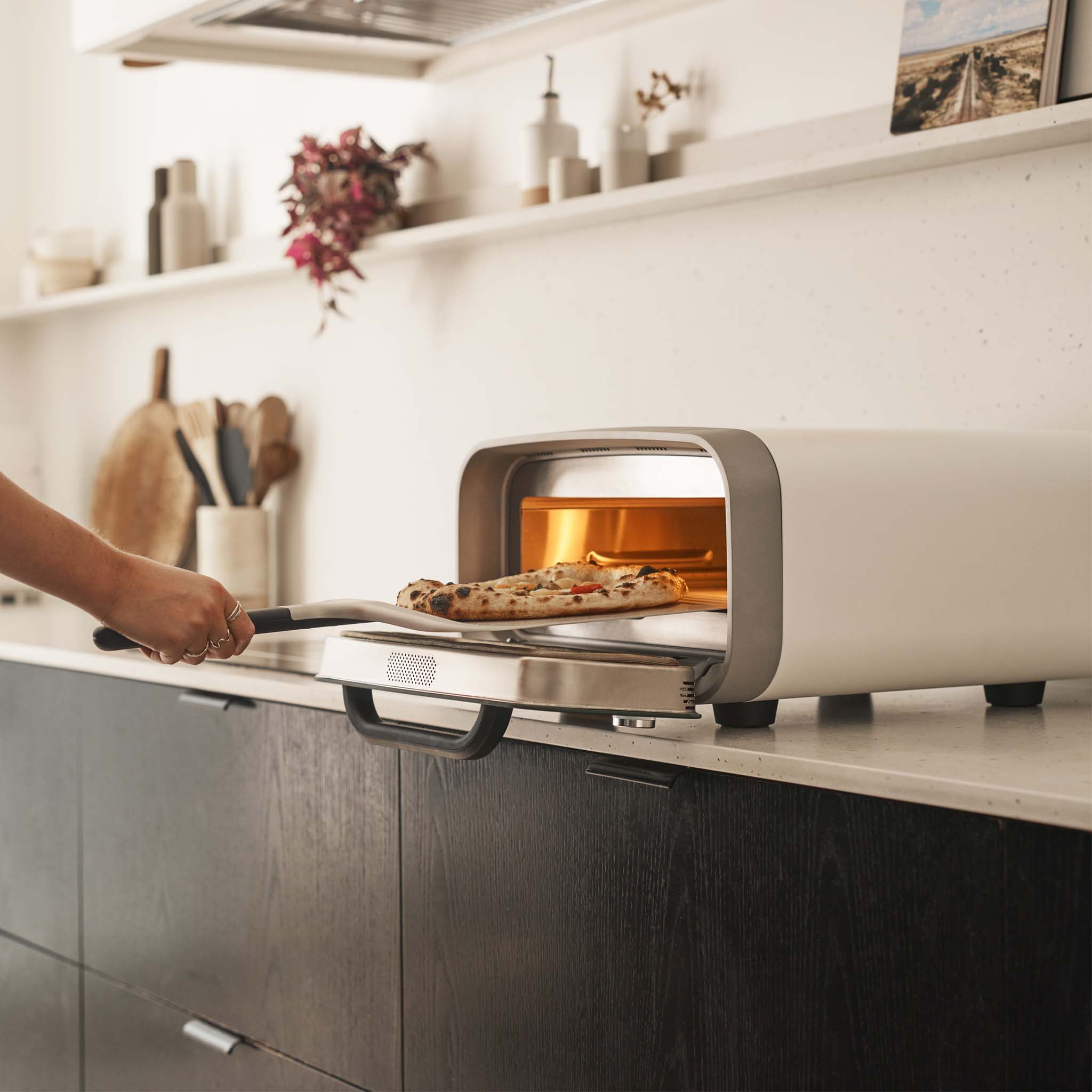 Person retrieving pizza from Ooni Volt 2 Electric pizza oven in a kitchen setting. 
