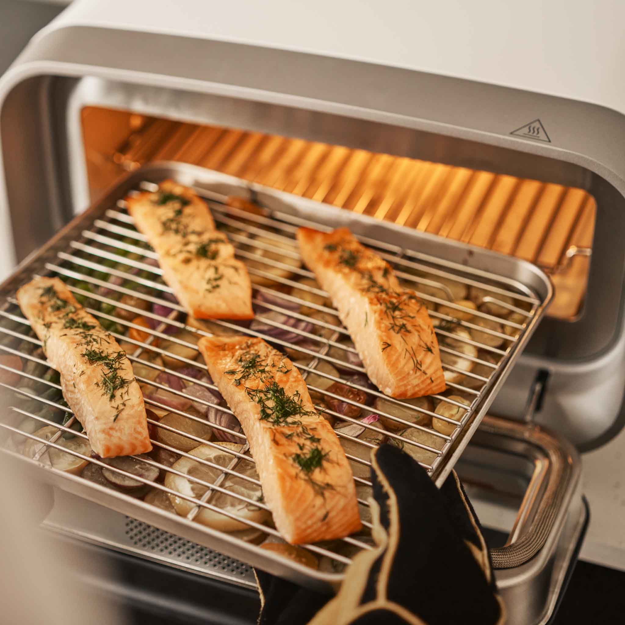 Baked salmon filets on an Ooni sheet pan and wire rack being retrieved from the Ooni Volt 2 electric pizza oven.