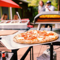 Cooked pepperoni pizza on top of pizza peel with Ooni Koda 16 in the background