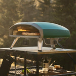 Gas powered ooni pizza oven in color highland green on a stand with a pizza inside, outdoors.