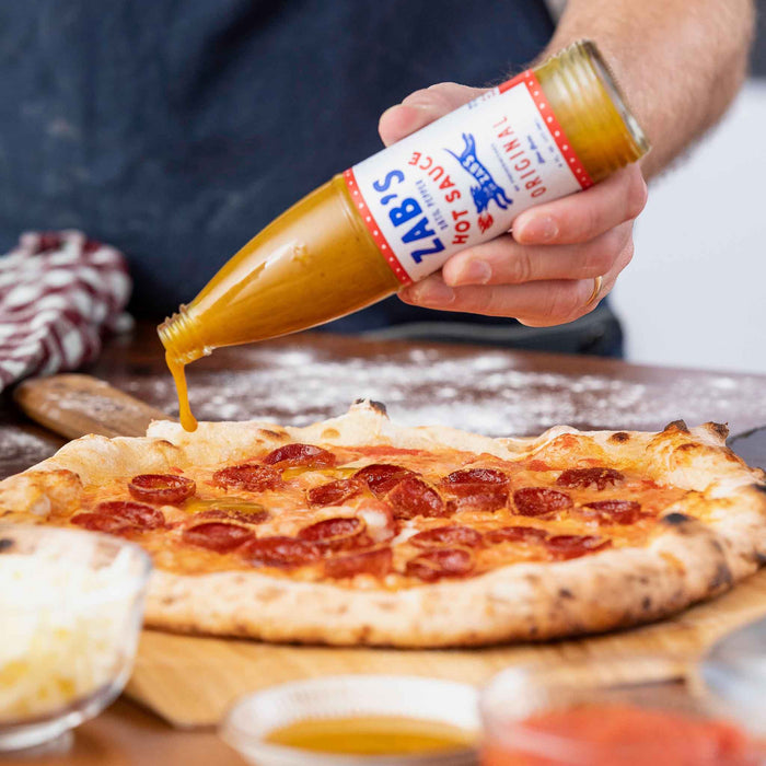 Zabs Original Hot Sauce drizzled on pepperoni pizza | Click this image to open up the product gallery modal. The product gallery modal allows the images to be zoomed in on.