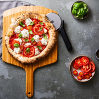 Cooked pizza on top of bamboo peel with Ooni cutter wheel underneath