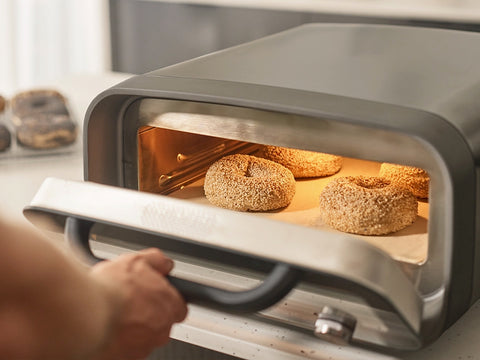 Person opening an Ooni Volt 2 electric pizza oven to reveal bagels inside